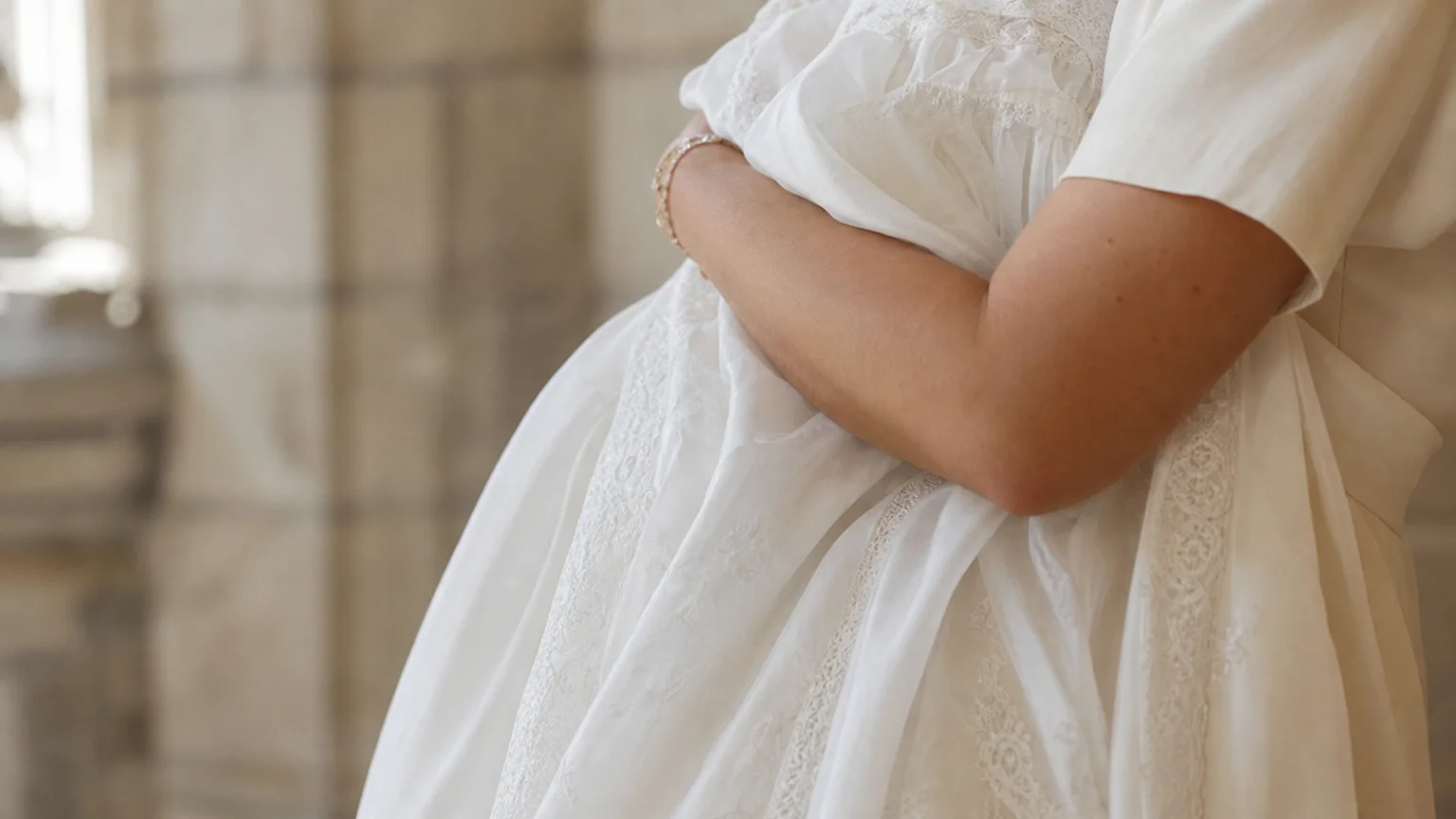 Bras d'une marraine tenant un bébé dans sa robe de baptême blanche