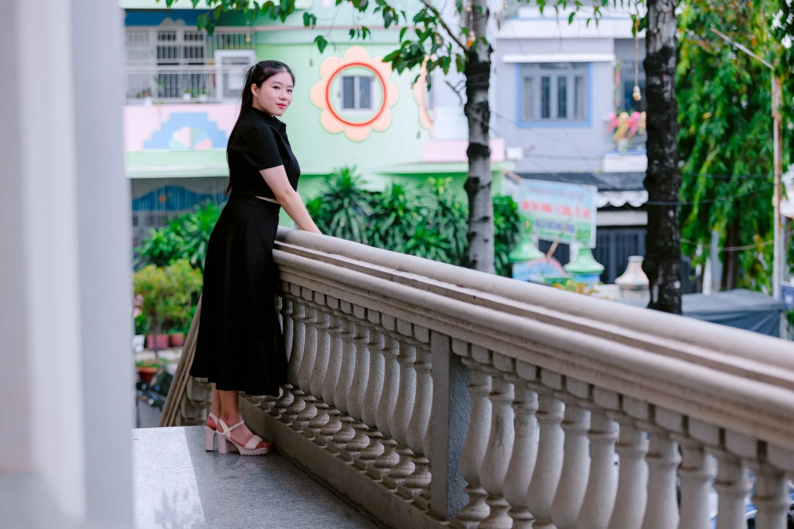 Robe noire midi portée en pied, silhouette allongée sur balustrade extérieure